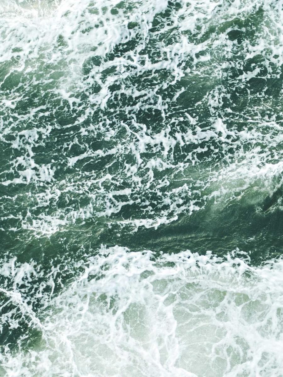 Espuma branca desenhando linhas sobre o mar verde-escuro, visto de cima