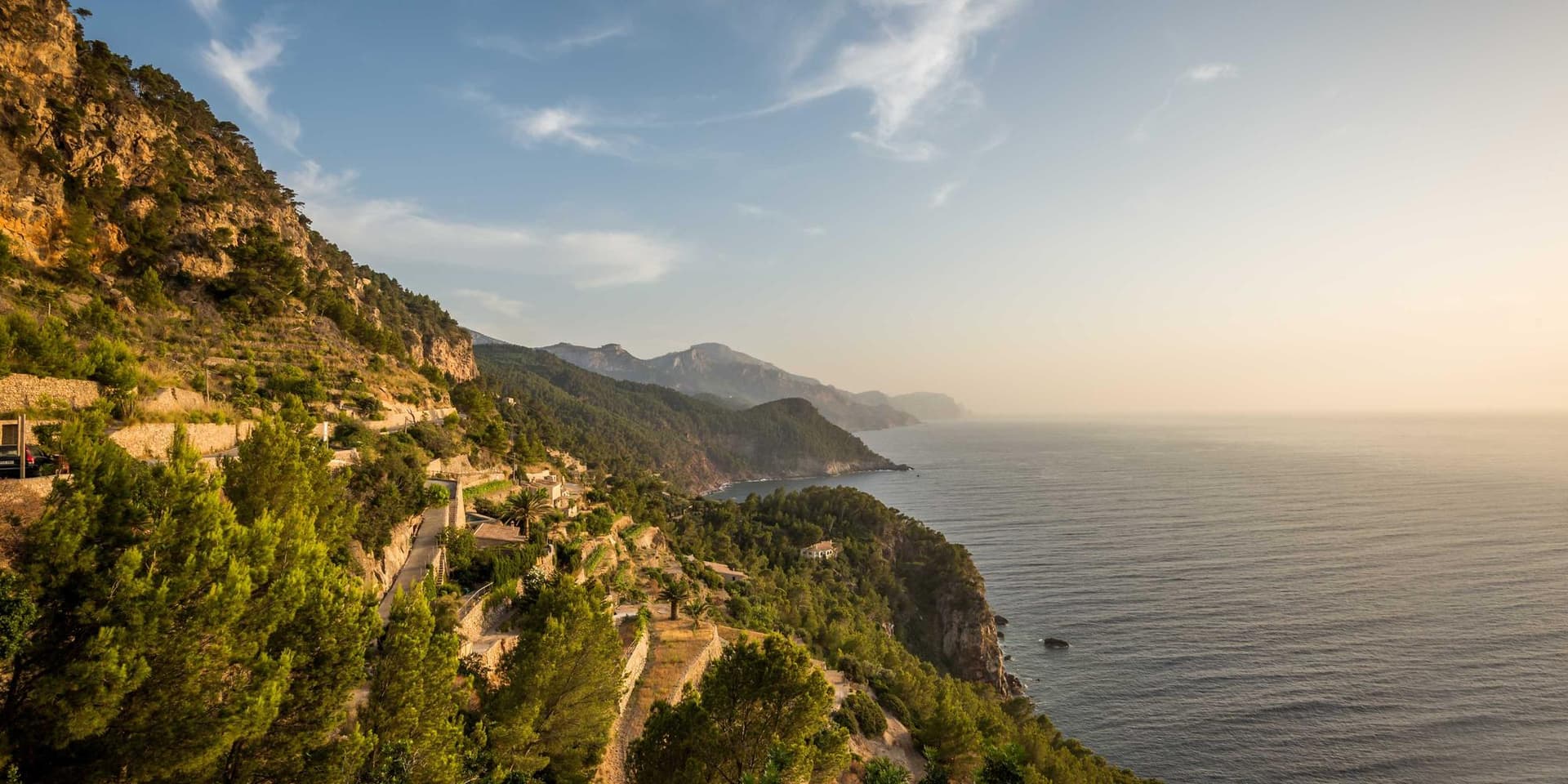 Encosta coberta de mata descendo até o mar, com estrada estreita cortando a montanha ao amanhecer