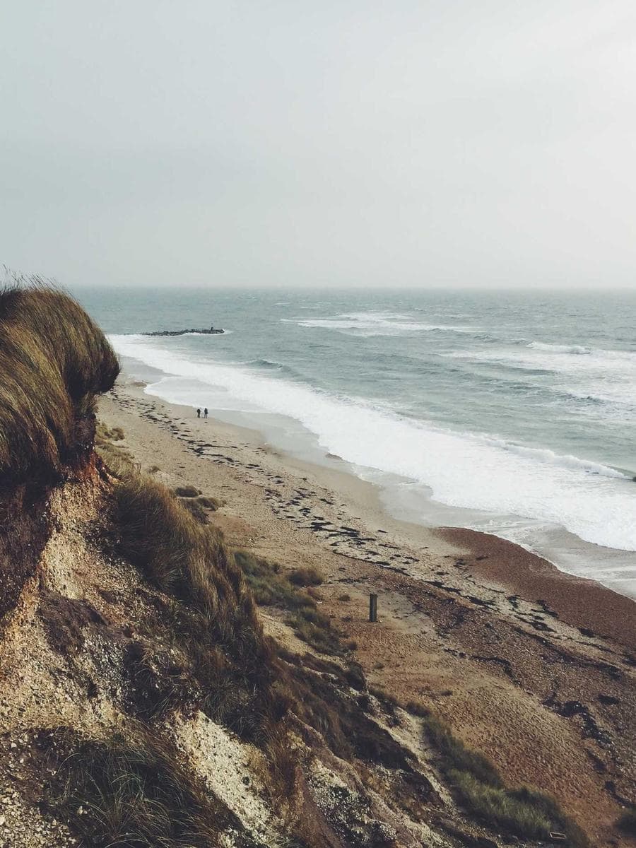 Duna erodida sobre uma praia vazia, com as ondas quebrando ao lado