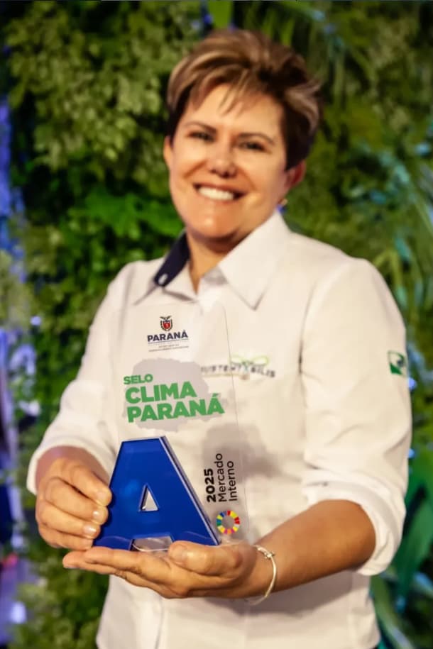 Isabela, da Sustentabilis, segurando o troféu do Selo Clima Paraná 2025 — nota A na categoria Mercado Interno